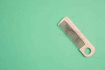 Wooden comb with lost hair on green background, top view. Space for text