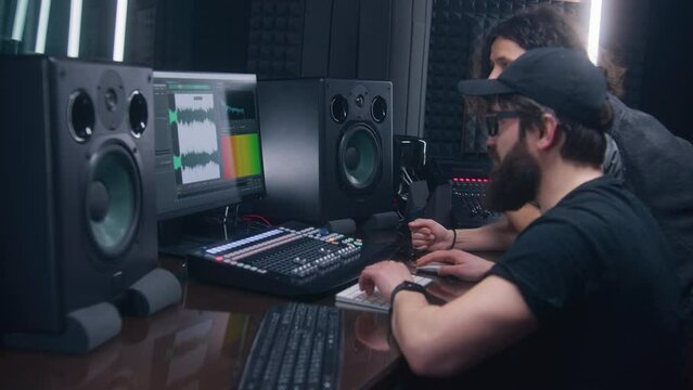 Sound engineer and musician create song in music recording room. Computer screen showing DAW software interface with sound track. Modern equipment in sound recording studio. Music production concept.