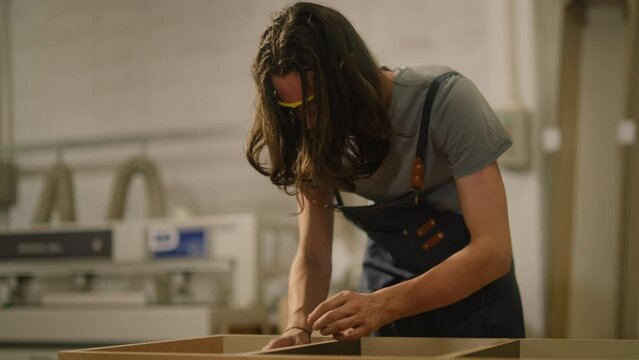 young hipster carpenter man tying his hair because his hair is blinding his eyes and making woodworks furniture in wood workshop.Carpenter SME owner at work measuring wooden by Cartridges Meters.