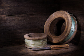 Two old wooden hand fishing reels lines rusty hooks fish scaling knife rustic wooden setting spotlight mood lighting 