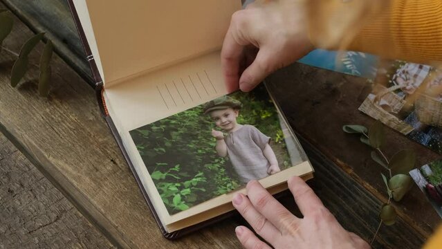 Female hands adding printed picture of joyful toddler to family photo album.