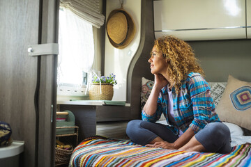 Travel lifestyle and dreaming people destination. One serene happy woman sitting on bed inside camper van bedroom and looking outside the window with dreamer expression. Freedom and independence life