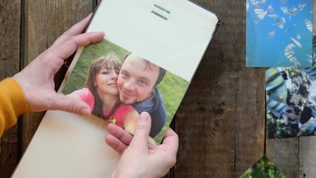 Female hands adding printed picture of happy couple to family photo album.