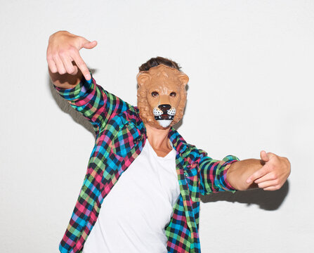Animal mask, hand gesture and a man in studio with cool attitude to party with a positive mindset. Lion face or male model person isolated on a white background for fun, funny and goofy portrait