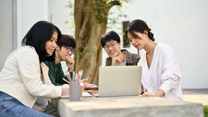 Group of happy Asian college students looking at a laptop screen, discussing their school project