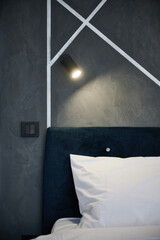 Bedroom interior with dark bed and white pillow, illuminated with bedside lamp. Crop view of...