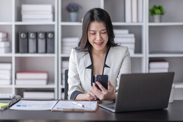 Cheerful business Asian woman freelancer making telephone call share good news about project working in office workplace, business finance concept.	