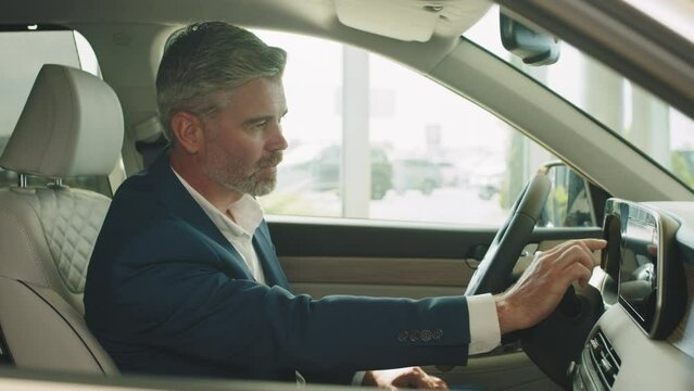 Male sitting in automobile cabin and testing new car, using screen of media platform, touching, pointing by finger. Successful businessman in formal wear sitting on driver's seat. Focus on eyes