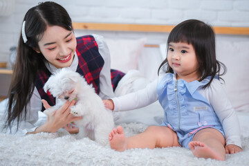 It's clear that the white dog brings joy and comfort to both the beautiful asian woman and the little girl as they spend time together on the bed in the bedroom.