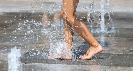 Girl's feet in the spray of a fountain in the park