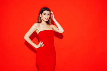 Young beautiful smiling female in trendy summer red evening dress. Sexy carefree brunette woman posing in studio, isolated. Positive model with evening makeup. Cheerful and happy