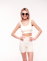 Young beautiful smiling blond female in summer cycling shorts clothes. Sexy carefree woman posing on white background in studio. Positive model having fun indoors. Cheerful and happy. In sunglasses