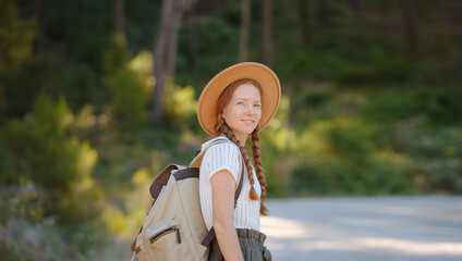 Caucasian ginger young beautiful female backpacker traveling alone in forest. Attractive traveler look around and explore while walk in nature wood with happiness and fun during holiday vacation trip.