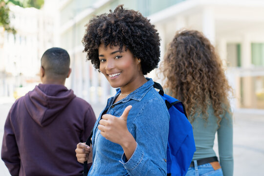 Successful black female student with backpack and friends showing thumb up