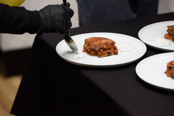 the chef in the restaurant preparing traditional greek moussaka in white plate on black tablecloth background