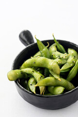 japanese edamame beans snack in black ceramic bowl on white background