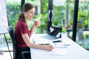 Smiling businesswoman holding coffee cup and working on laptop in office