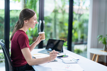 Smiling businesswoman holding coffee cup and working on laptop in office