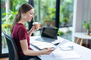 Smiling businesswoman holding coffee cup and working on laptop in office