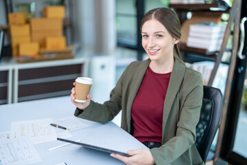 Fototapeta na wymiar Smiling businesswoman holding coffee cup and working on laptop in office