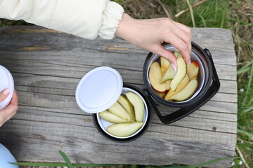 thermos for food and drinks for travel made of stainless steel with a black lid on a wooden bench on the bank of a mountain river. girl's hands hold a thermos. mountain tourism. for banners, flyers