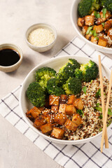 One quinoa bowl with steamed broccoli and smoked tofu cubes in teriyaki sauce with sesame seeds as topping on white checkered kitchen napkin, grey concrete background