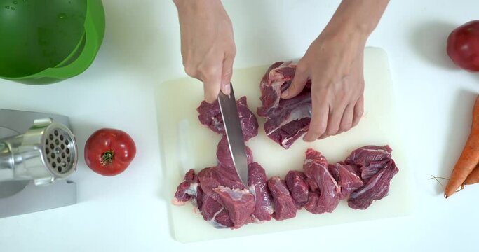 Close-up view of woman cutting up fresh meat with a knife on a kitchen board.
