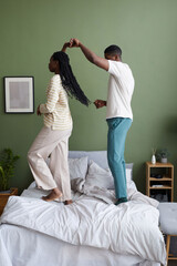 Vertical image of African American young couple dancing on bed in bedroom during their leisure time