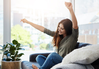 Celebrating my freedom. a happy young woman dancing while sitting on her sofa at home.