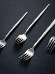 Stainless steel cutlery placed on a dark tabletop (cutlery), indoor photography light