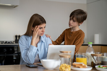 Busy mother freelancer trying to work from home with child, looking at laptop screen and trying to...