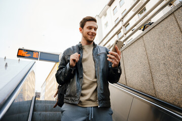 Man using smartphone while going down to subway on escalator