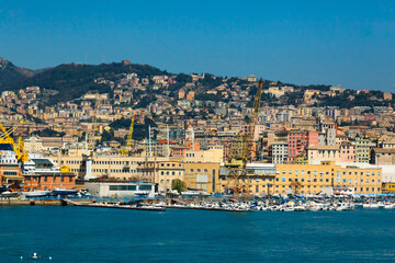 Fototapeta na wymiar Scenic view of the maritime city of Genoa in Italy. View from the sea to the Italian city of Genoa, beautiful colorful houses along the coast, harbor cranes and yachts moored at the pier.