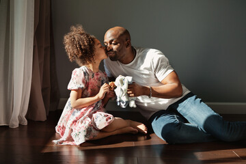 Happy African American father and his daughter playing toy together . Baby girl kissing dad sitting...