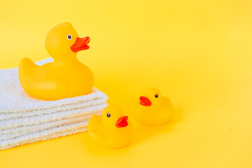 Stacked white towels and bath ducks on yellow background