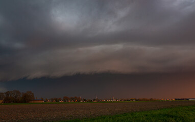 A shelf cloud of a severe thunderstorm rolls over the plains at sunset