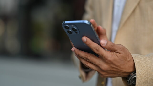 Cropped image of businessman texting messages, chatting in social on smartphone while standing outdoor