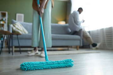 Close-up of housewife wiping floor with mop during housework in the living room