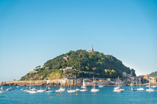 SAN SEBASTIAN, Spain July 08 2022: View of Santa Clara Island. Boats docked in the middle of La Concha Bay. Beautiful travel destination in north of Spain. Jesus Christ Statue on top of the hill.