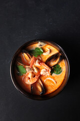 Tom Yam soup with coconut milk with shrimp, squid, mussels and mushrooms. Photo on a dark background. Flat lay. Top view. Copy space.
