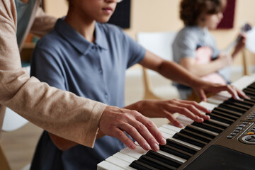 Close-up of schoolgirl learning to play piano together with teacher during musical lesson in class
