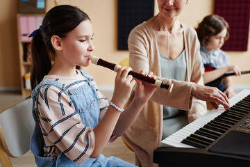 Schoolgirl playing flute with teacher playing piano during musical lesson in class © Seventyfour