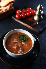 Traditional homemade sauerkraut soup. Bread croutons. Black background. Vertical photo.