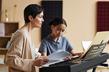 Music teacher teaching notes schoolgirl while she learning to play piano in music class