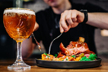 man cuts a pork knuckle with a knife and fork