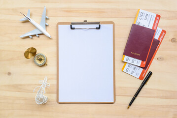 Top view of a blank white paper on a clipboard, decorated with a model airplane, a compass, a bicycle,a pen, two boarding pass and passports. Empty space for writing or noting a trip schedule or plan.