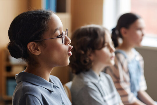 Side view of African American schoolgirl singing song together with other children in music class
