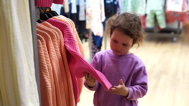 Cute child girl chooses clothes in shop store with clothes