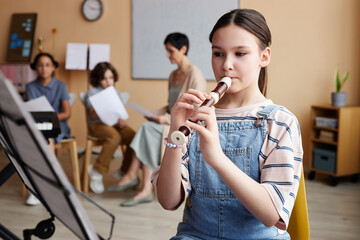 Schoolgirl sitting in front of sheet music and learning to play flute in music class