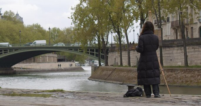 Female street art painter has some sketch practice with Paris city landscape. Experienced European woman artist draws new painting near the river. Painter and her lifestyle hobby leisure